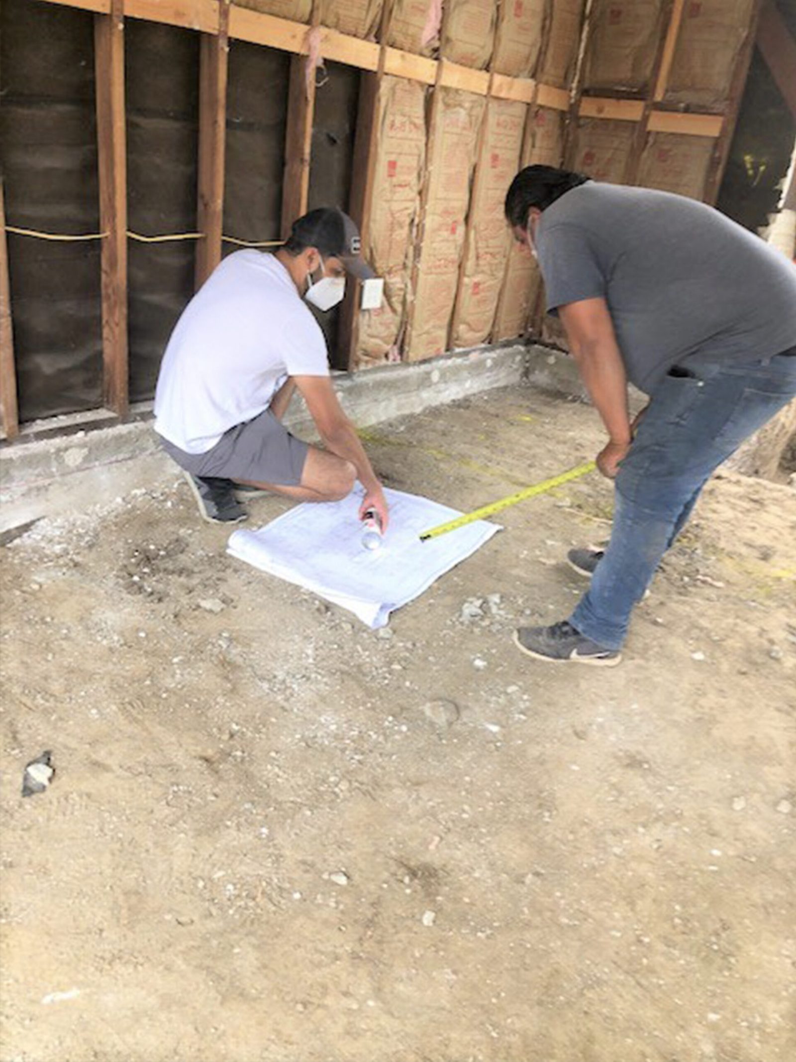 Two people measuring the garage floor with a plan and a tape measure